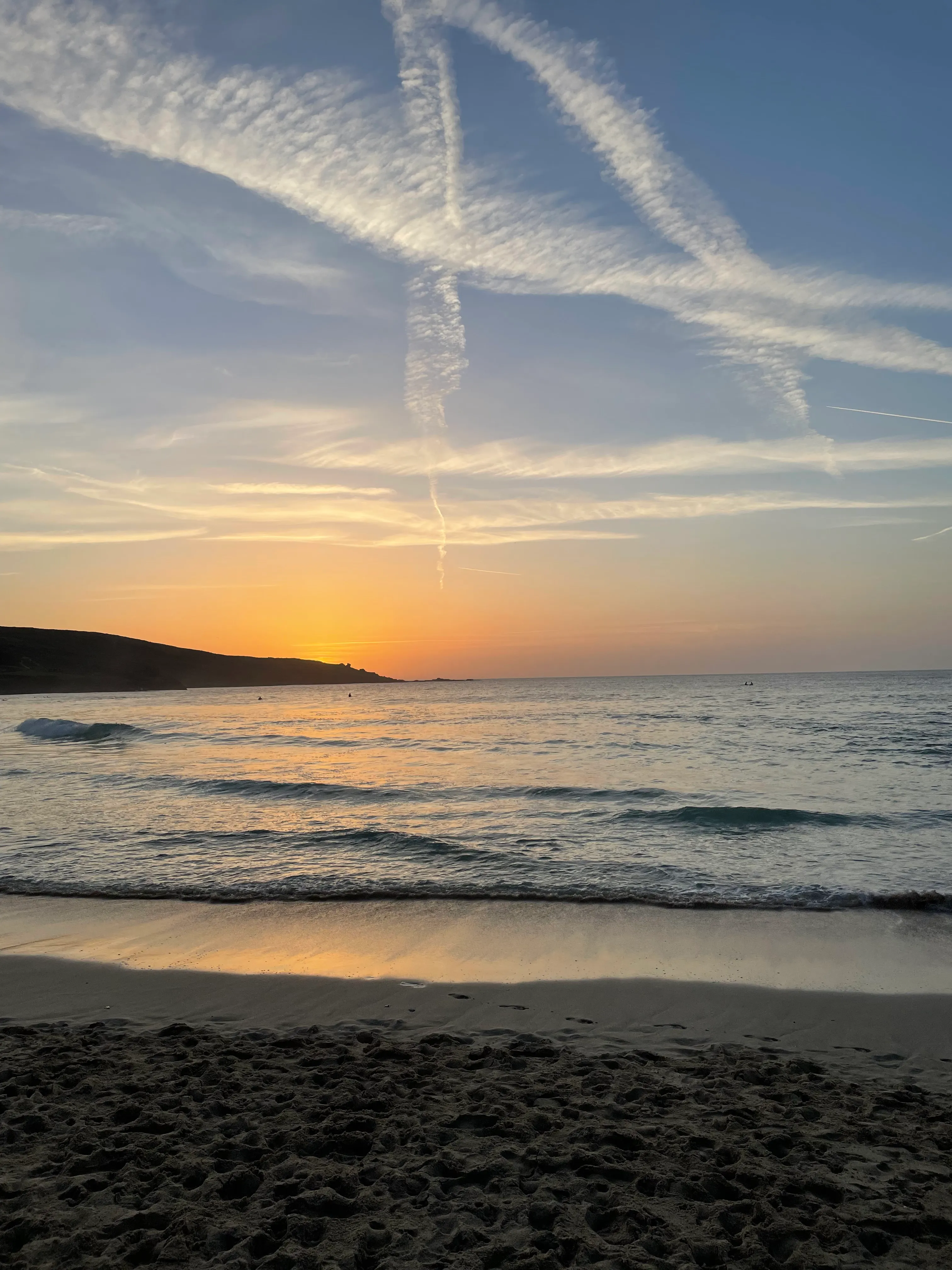 A quiet Cornish beach at sunset — soft waves rolling onto the sand under a sky streaked with golden light