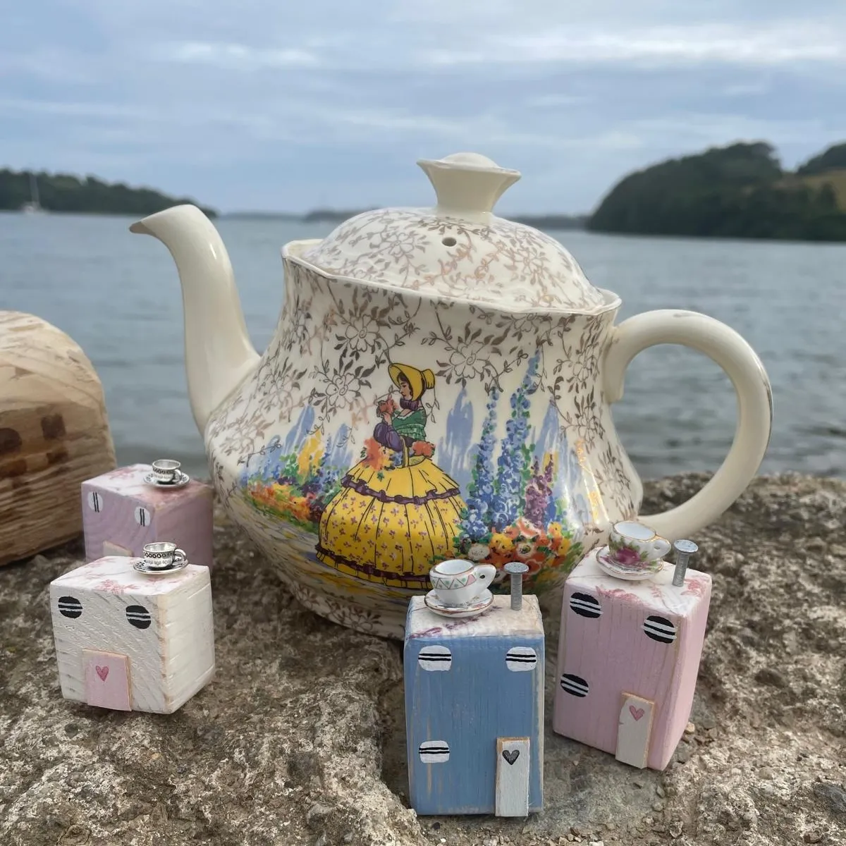 Tea by the Sea — a patterned teapot and tiny hand-painted wooden houses on a harbour wall